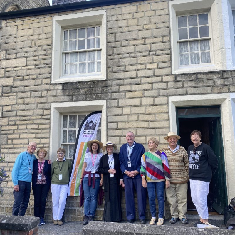 Volunteers stand outside of the Railway Village Cottage.